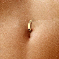 Minimalistische navelpiercing in goudkleur, afgebeeld in de navel