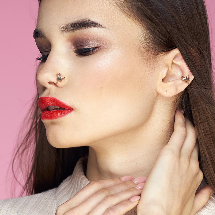 Vrouw draagt goudkleurige piercing in oor en neus met vlindertje voor subtiele look